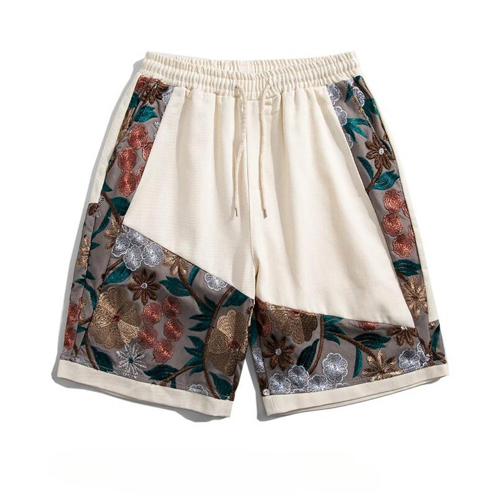 Cream-colored lightweight cotton shorts with an elastic waistband and drawstring, featuring decorative panels adorned with summer florals in brown, green, orange, silver, and gray tones.