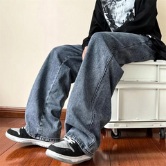 A person wearing relaxed fit, wide-legged blue jeans in a vintage wash, black and white sneakers, and a black long-sleeve shirt sits on a white storage box against a beige wall and wooden floor.