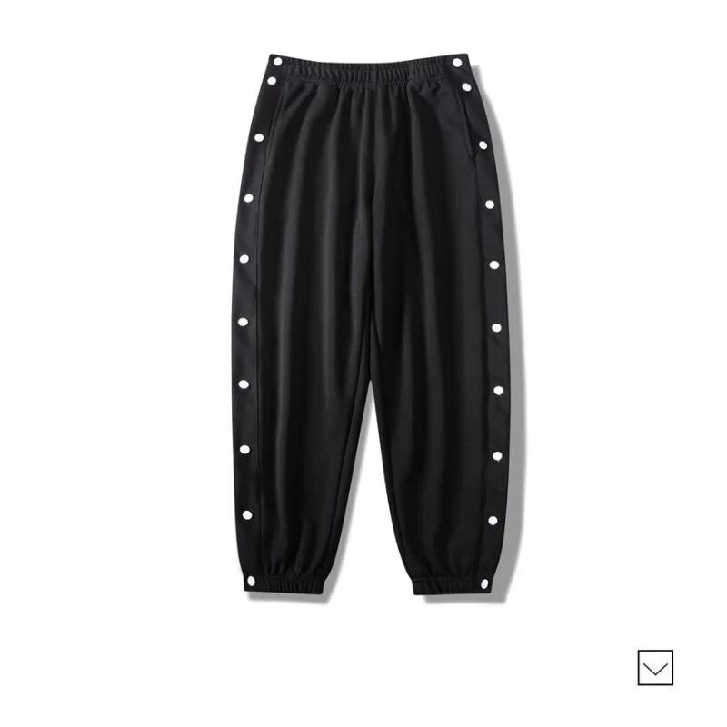 Black gym pants with an elastic waistband and cuffs, featuring white snap buttons along the outer sides of both legs. Made from moisture wicking fabric, the pants are laid flat on a white background.