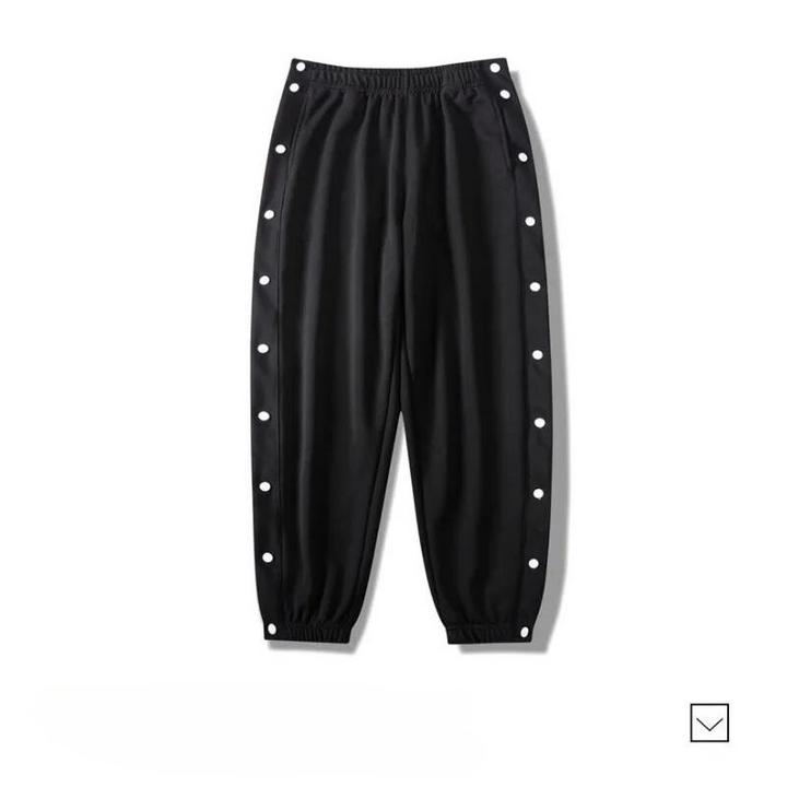 Black gym pants with an elastic waistband and cuffs, featuring white snap buttons along the outer sides of both legs. Made from moisture wicking fabric, the pants are laid flat on a white background.