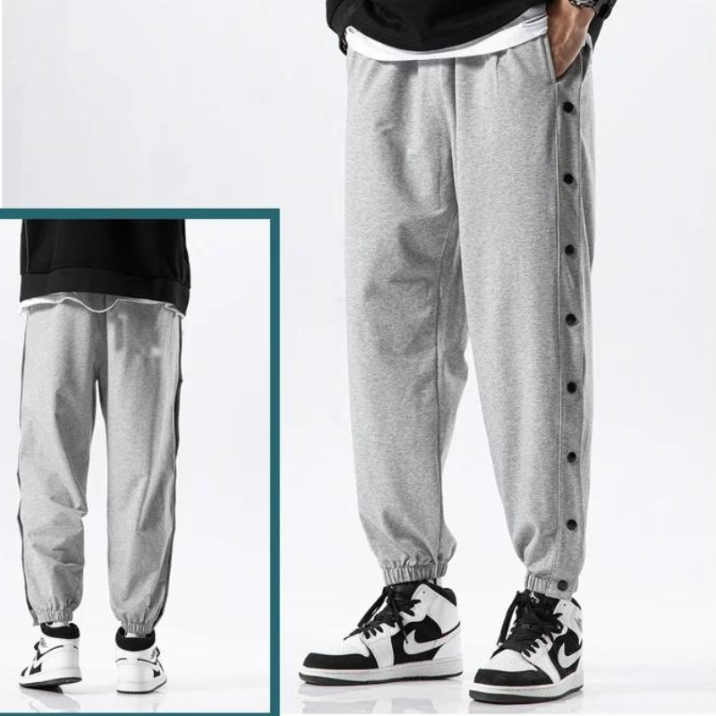 A person wearing grey button-up gym pants with black snap buttons down the sides, paired with white and black sneakers. An inset shows a rear view of the pants, made from moisture wicking fabric, and sneakers.