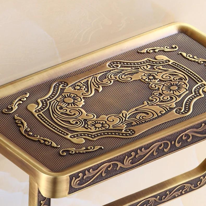 An ornate, rectangular brass table with an antique brass finish features intricate floral and swirl engravings on the top and sides, showcasing a luxurious design perfect for enhancing your bathroom decor.