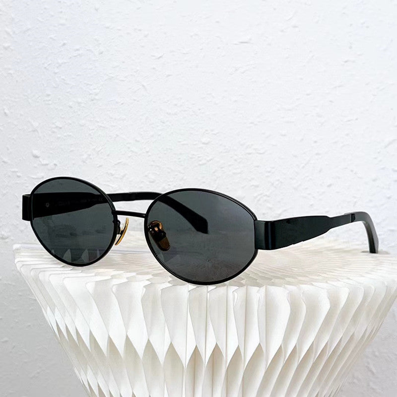 A pair of vintage-inspired, oval black sunglasses with dark UV400 protection lenses rests on a white, geometric textured surface against a white wall.