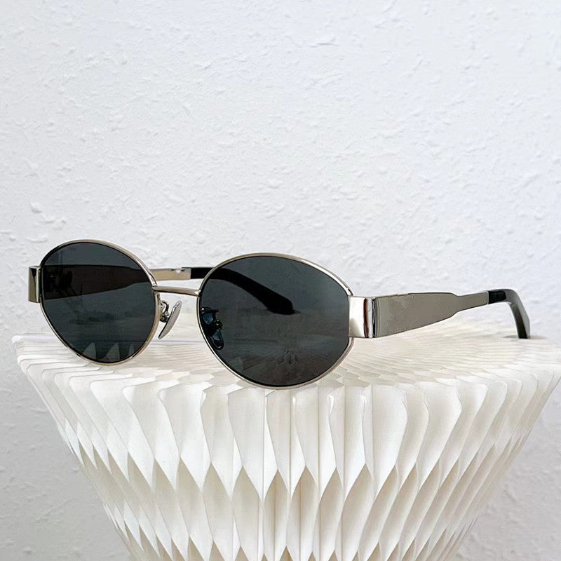 Silver-framed, round black vintage-inspired sunglasses rest on a white, textured, geometric surface against a plain white wall background.