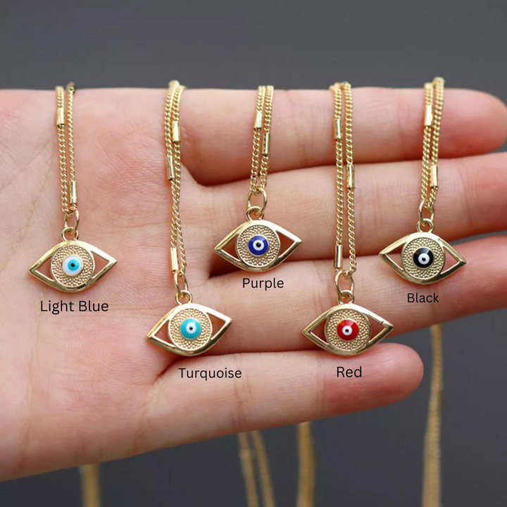 A hand holds four gold evil eye necklaces with pendants featuring zirconia stone centers in light blue, purple, black, and red. The colors are labeled beneath each pendant.