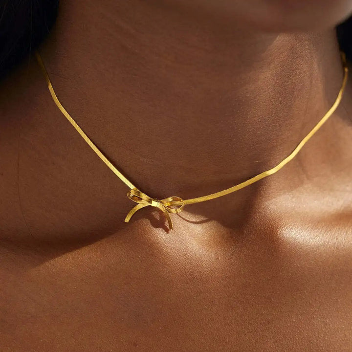 A close-up of a person wearing a thin gold bow necklace, a perfect piece of minimalist jewelry. The delicate bow pendant rests lightly on their bare skin, adding an elegant touch to any look.