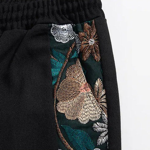 Close-up of black fabric with colorful embroidered summer florals in shades of brown, green, white, and teal, near an elastic waistband—possibly from lightweight cotton shorts or a skirt.