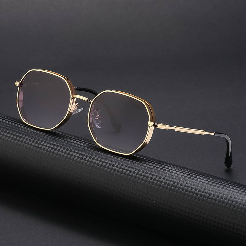 A pair of vintage-inspired sunglasses with gold-tone frames, dark lenses, and black temple tips is displayed on a textured black surface against a dark background.