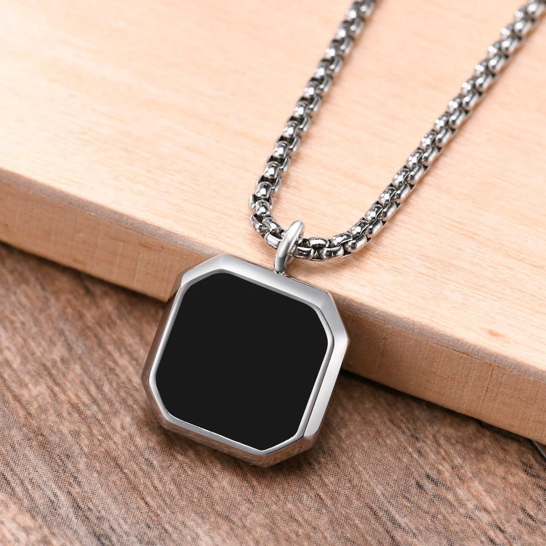 A silver chain necklace with a large, black, octagonal Onyx Stone Amulet pendant rests on a wooden surface—a striking piece for any collectable jewelry enthusiast.