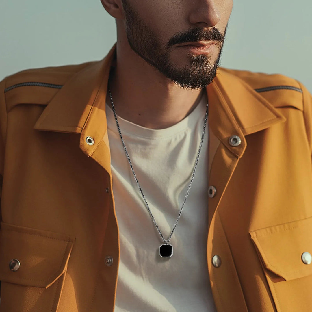 A man with a trimmed beard wears a yellow jacket over a white shirt and a collectable jewelry piece—a silver necklace with an Onyx Stone Amulet. The image is cropped to show his upper torso and part of his face.