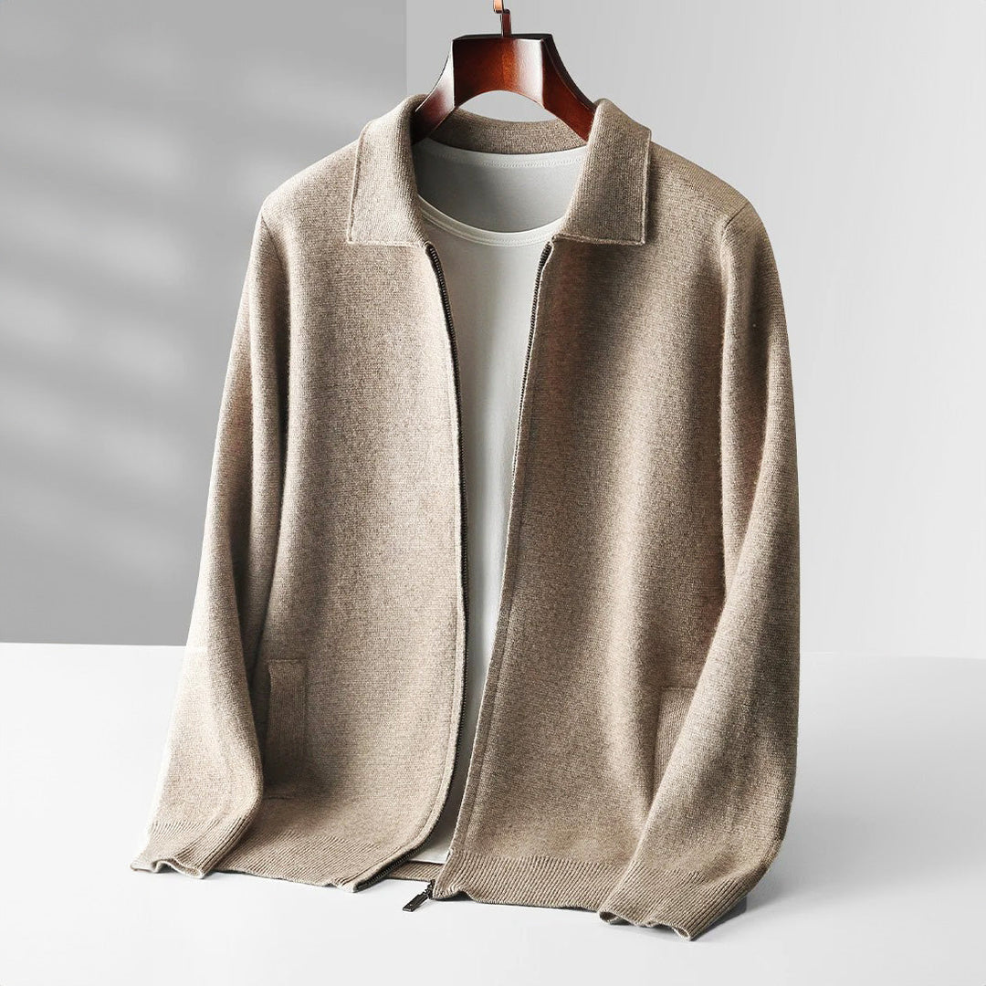 A beige merino wool zip-up cardigan with a collar is layered over a white crew-neck shirt, displayed on a wooden hanger against a minimal, light gray background.