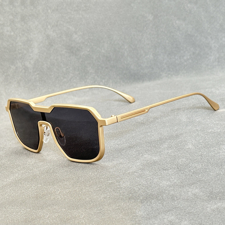 A pair of Steampunk Sunglasses with bold, geometric gold square frames and dark, oversized lenses rests on a gray textured surface.