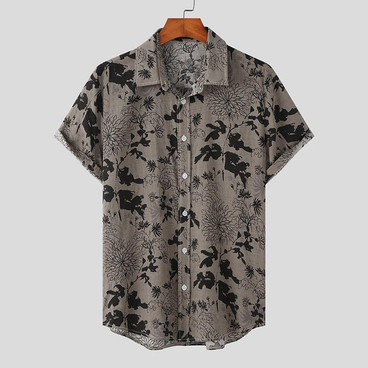 A short-sleeved, button-up Mens Hawaiian Shirt with a collar, featuring a grey background and black flower prints, displayed on a wooden hanger against a plain light grey background—a classic piece for streetwear fashion lovers.